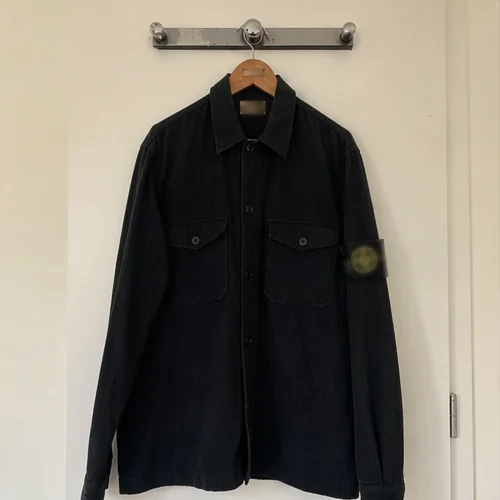 Veste Stone Island noire suspendue sur cintre contre une porte claire